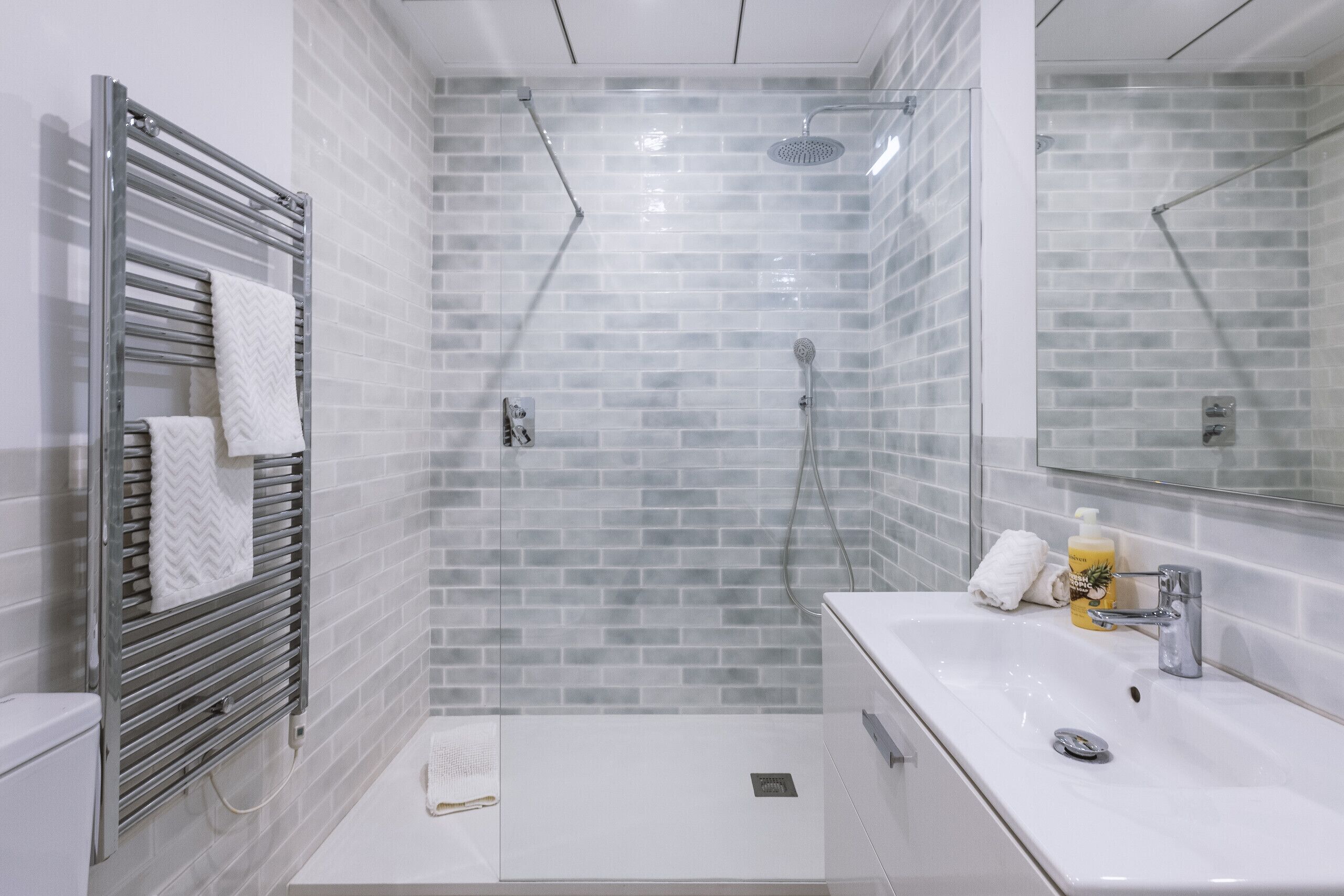 A modern bathroom with a glass shower enclosure, a white sink, and a towel rack.