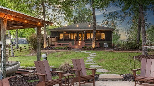 A cozy outdoor seating area with Adirondack chairs and a fire pit, a covered porch with string lights, and a house with a front porch and steps leading to the entrance.