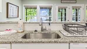 A kitchen with a granite countertop, stainless steel sink, and a view of the outdoors through large windows.