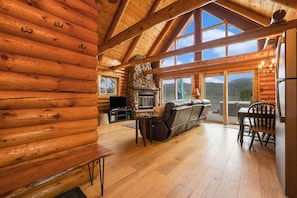 Ein Blockhaus-Interieur mit Kamin aus Naturstein, einem Holzespeisesaal und großen Fenstern mit Blick auf die Berge.