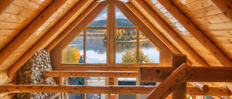 Ein Holzinnenraum mit einem großen Fenster mit Blick auf einen See und Herbstbäume.