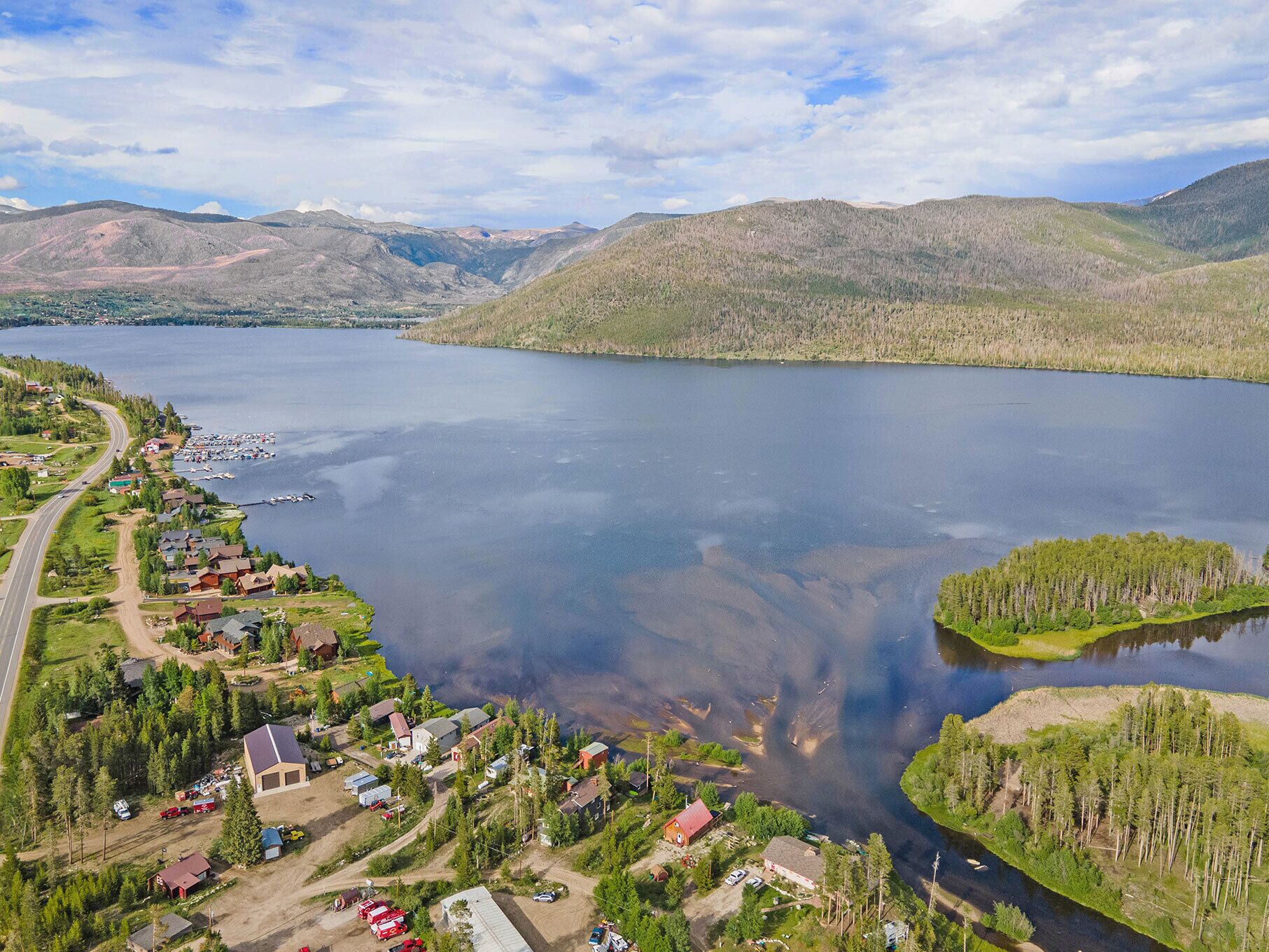 An aerial view of a lakeside community with houses, a dock, and surrounding hills.