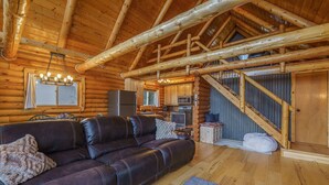 A log cabin interior with a wooden staircase, a kitchen area, and a leather sofa.