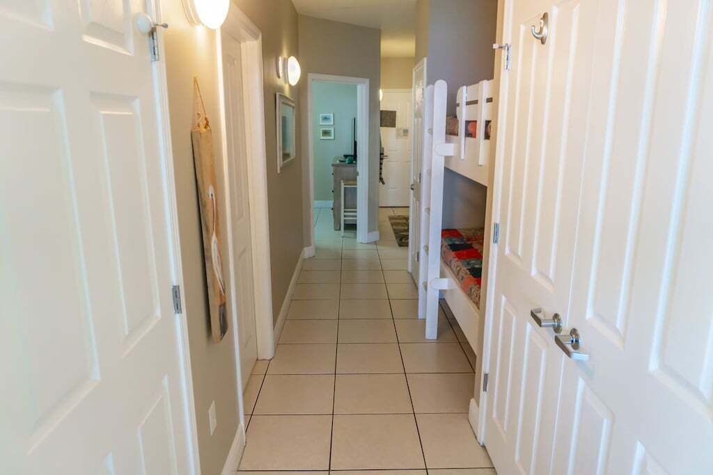A hallway with white doors, a tiled floor, and a bed with a red blanket.