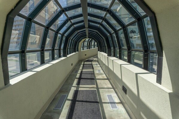 A corridor with a glass ceiling and walls, leading to a building entrance.