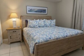 A bedroom with a wooden bed, a nightstand with a lamp, and a framed picture on the wall.