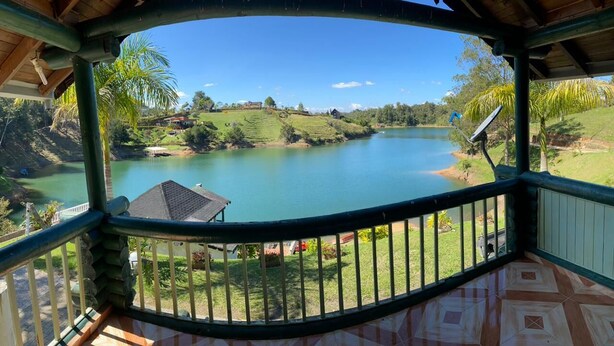 A covered balcony with a view of a lake, a house, and surrounding greenery.