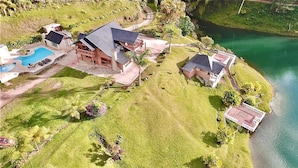 An aerial view of a property with a large house, a swimming pool, and a dock by a lake.