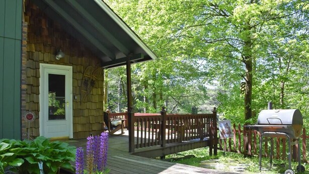 A wooden deck with a covered porch, a barbecue grill, and a stone building with a door.