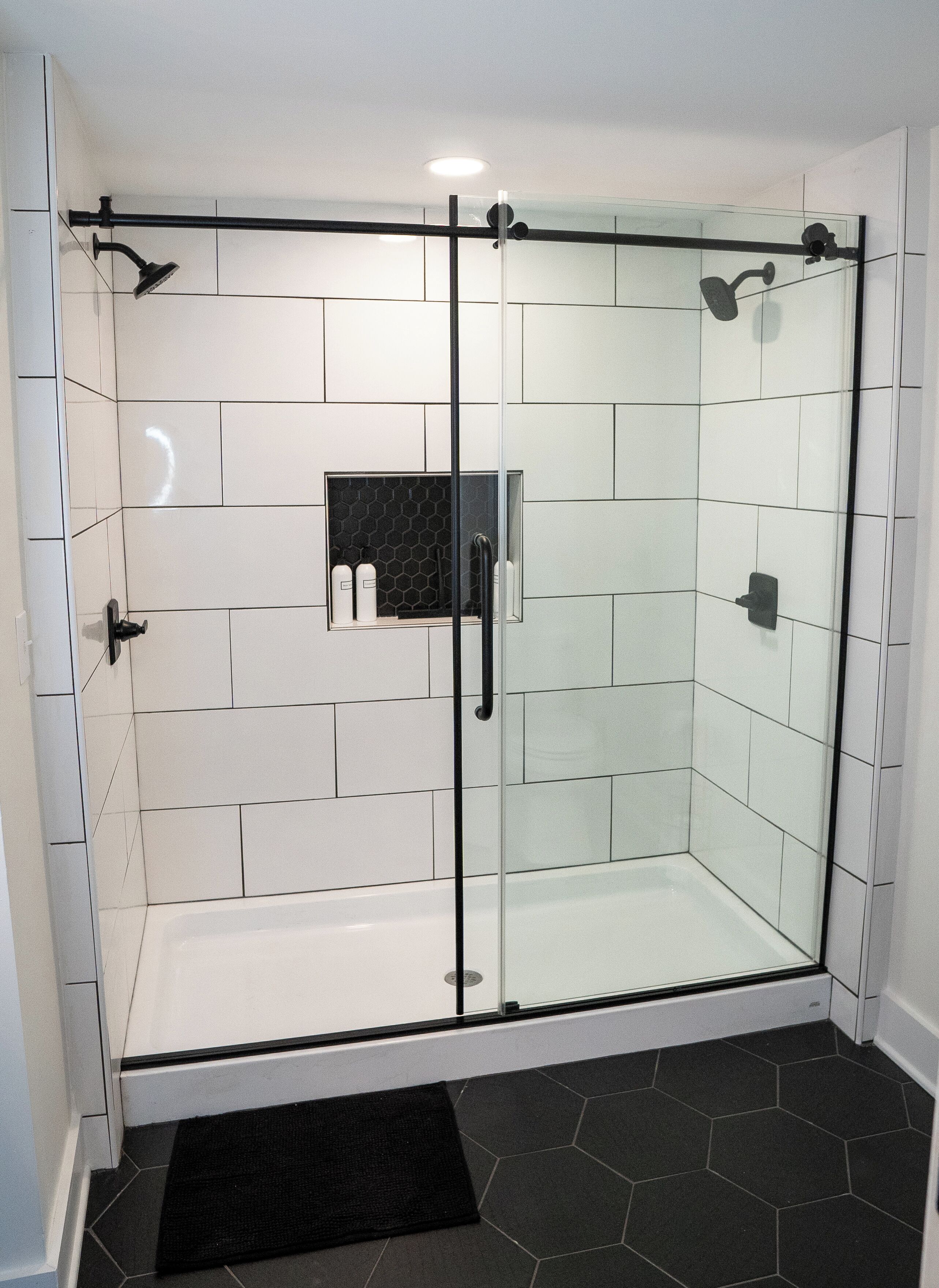 A glass-enclosed shower with white tiles, a black showerhead, and a black towel rack.
