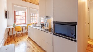 Una cocina moderna con suelo de madera, armarios blancos, microondas integrado y comedor con sillas amarillas.