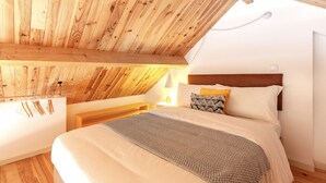 Un dormitorio con techo inclinado, vigas de madera, una cama con manta estampada y una mesita de noche con lámpara.