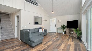 Un salon spacieux avec un canapé d’angle gris, un plancher en bois, un téléviseur à écran plat et un escalier menant à un autre niveau.