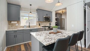 Une cuisine moderne avec des meubles gris, un îlot en granit et des tabourets de bar.