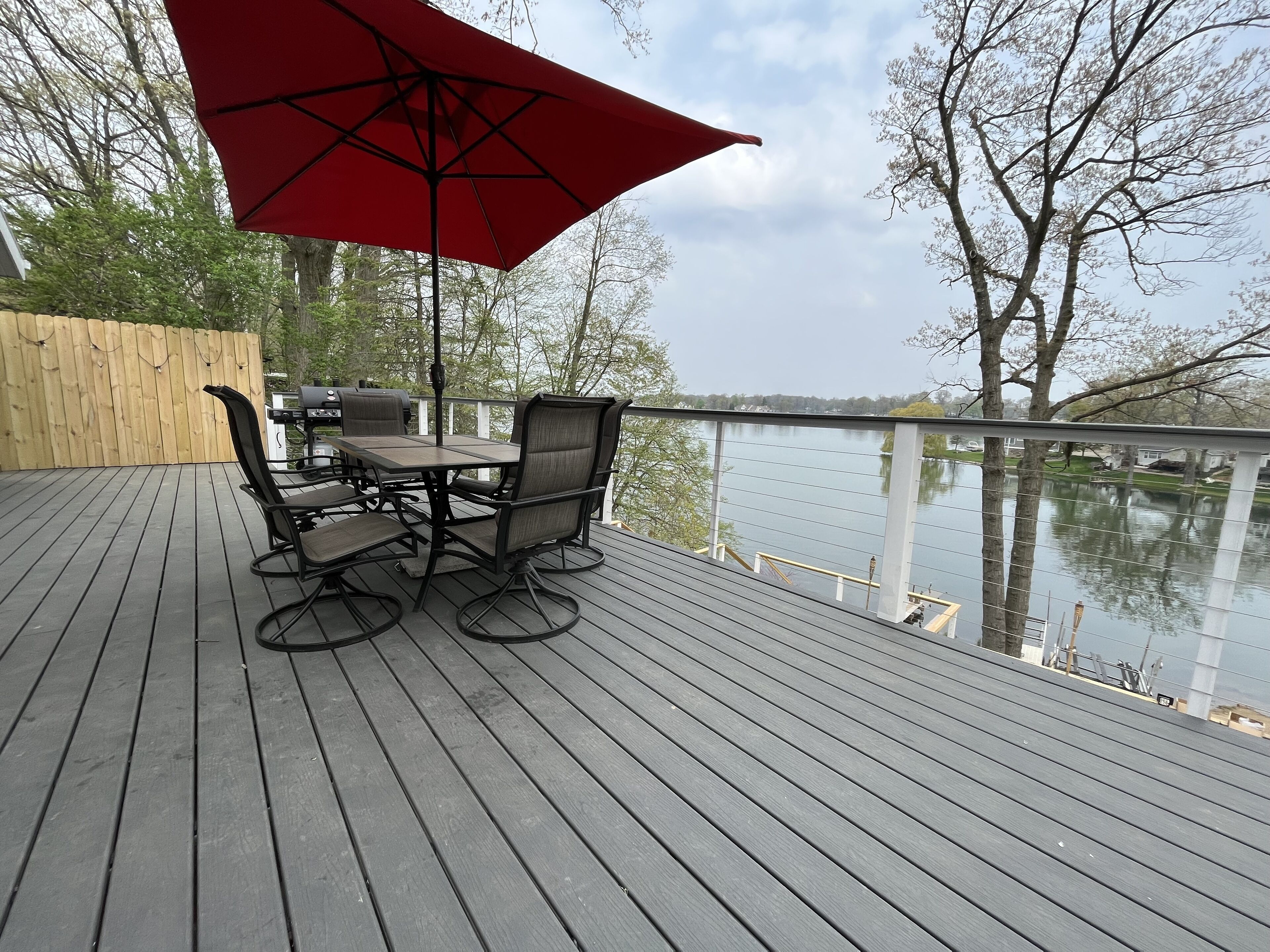 A deck with a table and chairs, a red umbrella, and a view of a lake.
