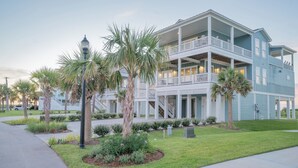 A two-story building with a balcony on the second floor, surrounded by a well-maintained lawn and palm trees. - Pointe West Beach Custom Home, Beach to Bay views, PW Pool/Private Beach (Galveston)