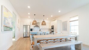 A modern kitchen with white cabinets, a stainless steel refrigerator, a large dining table, and pendant lights. - Pointe West Beach Custom Home, Beach to Bay views, PW Pool/Private Beach (Galveston)