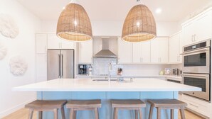 A modern kitchen with a large island, stainless steel appliances, and wooden stools. - Pointe West Beach Custom Home, Beach to Bay views, PW Pool/Private Beach (Galveston)