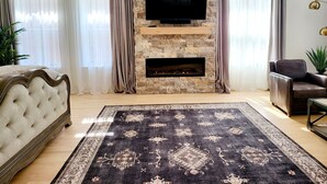 Una sala de estar con chimenea de piedra, televisor de pantalla plana, sofá y alfombra estampada.