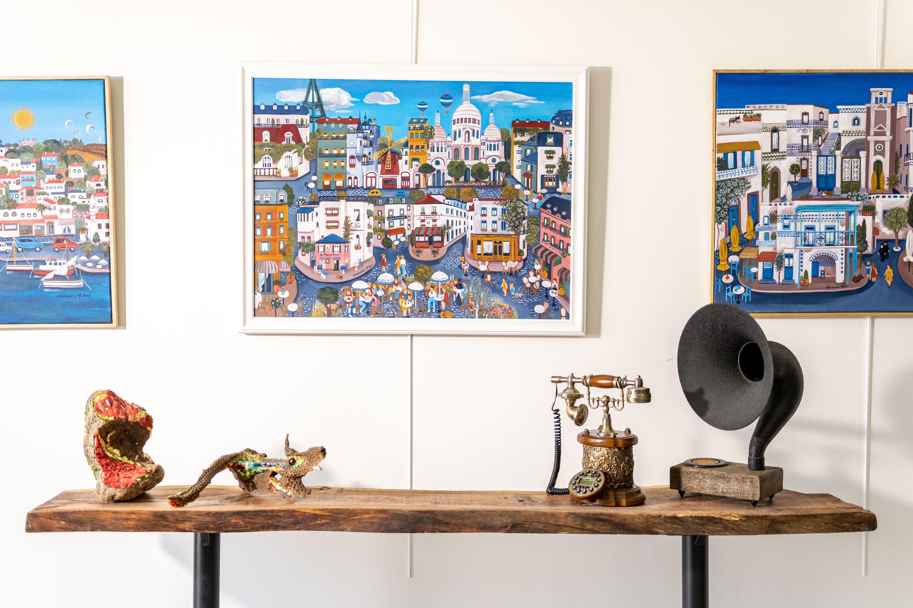 Una mesa con un teléfono antiguo, una escultura y un cuadro enmarcado de un paisaje urbano.
