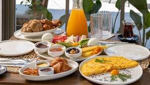 A breakfast table with various dishes, a glass of orange juice, and a view of outdoor seating.