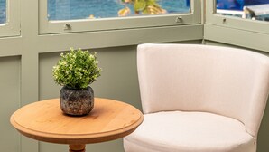 A room with a view of the sea, a chair, and a small table with a plant.