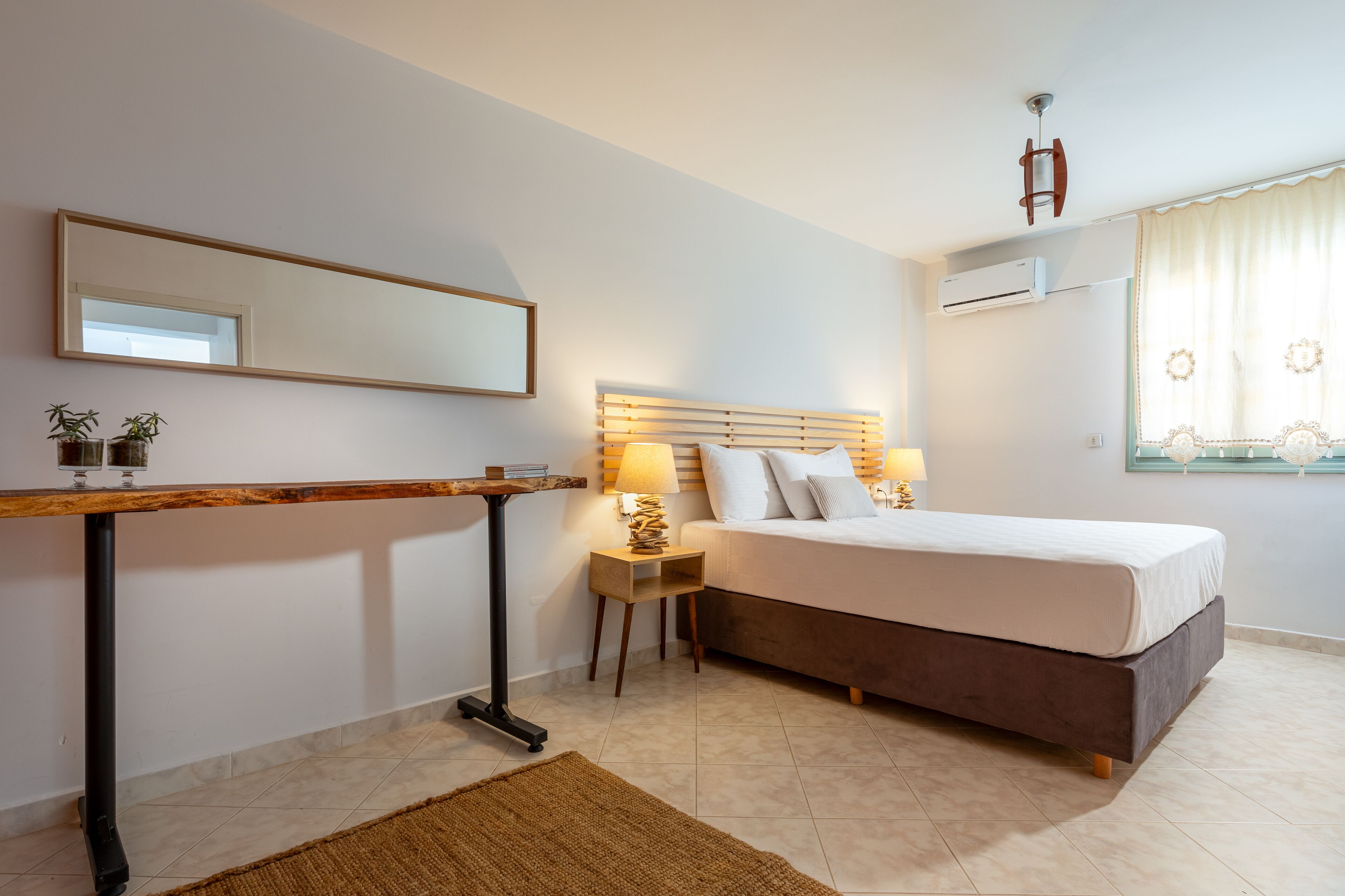 A bedroom with a bed, bedside table, lamp, and a mirror.