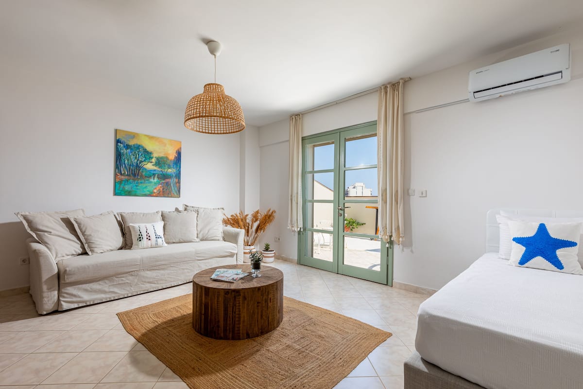 Habitación de hotel moderna con sofá, una mesita de centro redonda de madera, una cama con almohada con forma de estrella, un cuadro en la pared y un equipo de aire acondicionado.