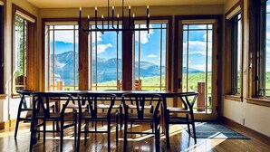 A dining area with a wooden table and chairs, large windows with a mountain view, and a hanging light fixture. - Goldlink Lodge (Crested Butte)