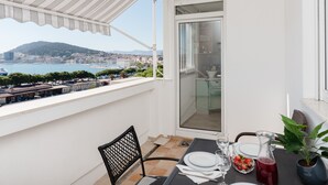 Un balcon avec une table dressée pour deux personnes, offrant une vue sur le paysage urbain de la côte.