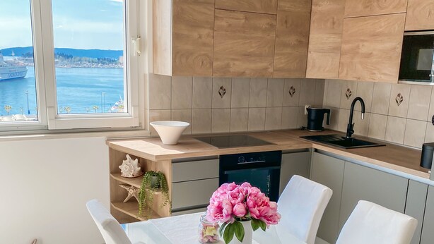 Une cuisine moderne avec des meubles en bois, un four encastré et une fenêtre donnant sur un plan d’eau.