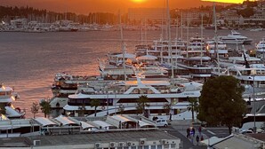Un port de plaisance avec des bateaux amarrés, un coucher de soleil en arrière-plan et une vue sur la ville de l’autre côté de l’eau.