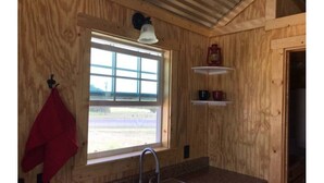 A wooden cabin kitchen with a window, sink, and a red towel hanging on the wall.
