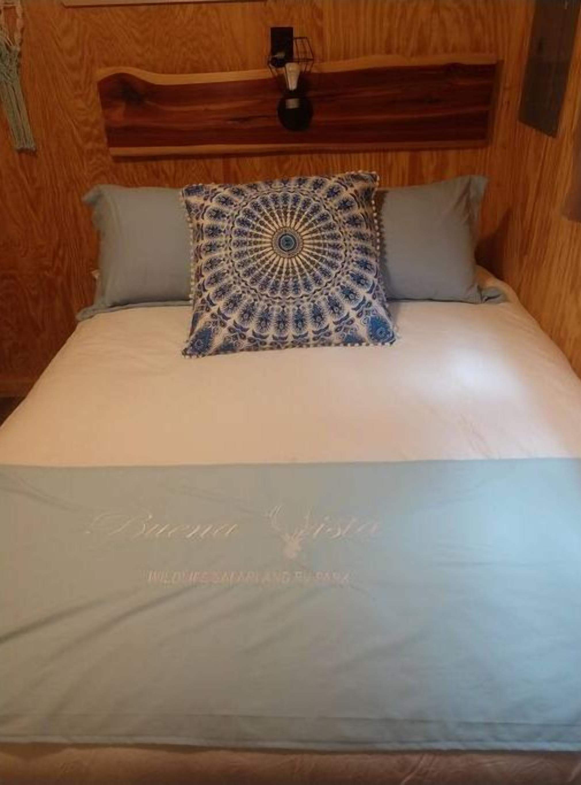 A bed with a blue and white patterned pillow, a light blue bedspread, and a wooden headboard.