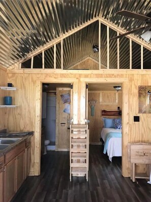Una cabaña de madera acogedora con un altilocte, una cocina con lavamanos y una escalera que sube al altilocte.