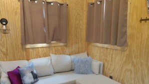 Une pièce chaleureuse avec un canapé d’angle beige, un mur en bois et une fenêtre ornée de rideaux bruns.