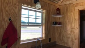 L’intérieur d’une cabane en bois comprend un coin cuisine équipé d’un évier, d’une fenêtre et d’une serviette rouge accrochée au mur.