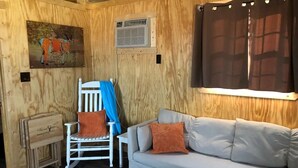 Une pièce chaleureuse avec un canapé blanc, un fauteuil blanc recouvert d’une housse bleue et un mur en bois orné d’une carte et d’un appareil de climatisation.
