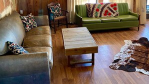 Un salon chaleureux avec un canapé vert, un fauteuil en cuir et une table basse en bois.