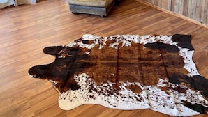 Une pièce aux murs en bois, avec un fauteuil en cuir, un téléviseur et une grande peau de vache servant de tapis.