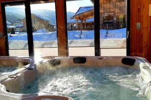 A hot tub with a view of a snowy mountain landscape and wooden buildings.