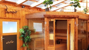 Eine Holzsauna mit Glastür, Blumentopf und Bergmotiv auf der Tür.