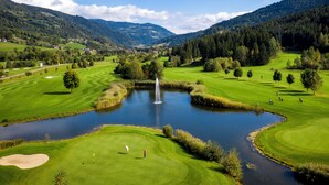 Ein Golfplatz mit Teich, Bäumen und einer Bergkulisse.