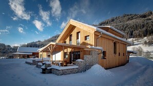 Eine Holzhütte mit Steinunterbau, großen Fenstern und verschneiter Landschaft.