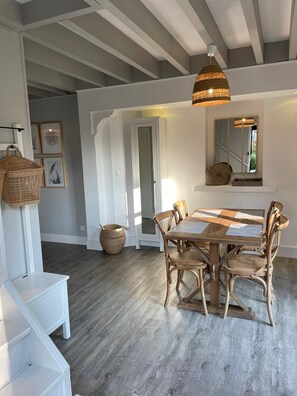 A dining area with a wooden table and chairs, a hanging light fixture, and a mirror on the wall.