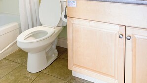 A bathroom with a toilet, a shower curtain, a sink with a mirror, and a window above the toilet. - Parlee Beach Motel (Shediac)