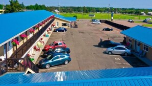 A motel with a blue roof, a parking lot, and a row of rooms with balconies. - Parlee Beach Motel (Shediac)