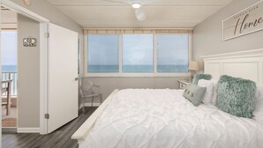 Ein Schlafzimmer mit einem großen Bett, einem Deckenventilator, einem Fenster mit Ausblick, einem Nachttisch mit Lampe und einem Schild an der Tür.