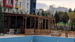 A swimming pool with a wooden deck and a covered seating area. - Luxury Apartment in Tbilisi | 24/7 Security | Prime Location (T'bilisi)
