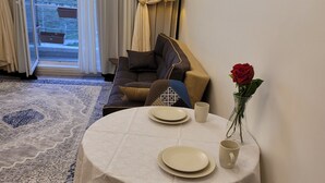 A dining area with a round table set for two, a colorful chair, a vase with a red rose, and a view of the outdoors through a sliding door. - Luxury Apartment in Tbilisi | 24/7 Security | Prime Location (T'bilisi)